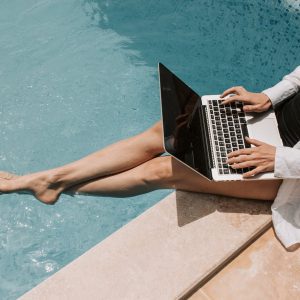 woman sitting on poolside using laptop