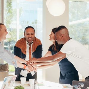smiling multiracial coworkers with hands together in office