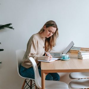 focused woman writing in notebook at table with laptop