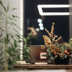 a pot of plant with christmas decorations beside a laptop on a wooden table