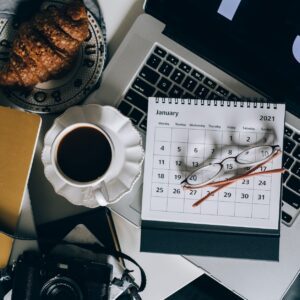 calendar on a laptop beside a cup of black coffee