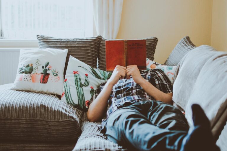Relaxing at home, lying on a sofa with a book and cushions around.