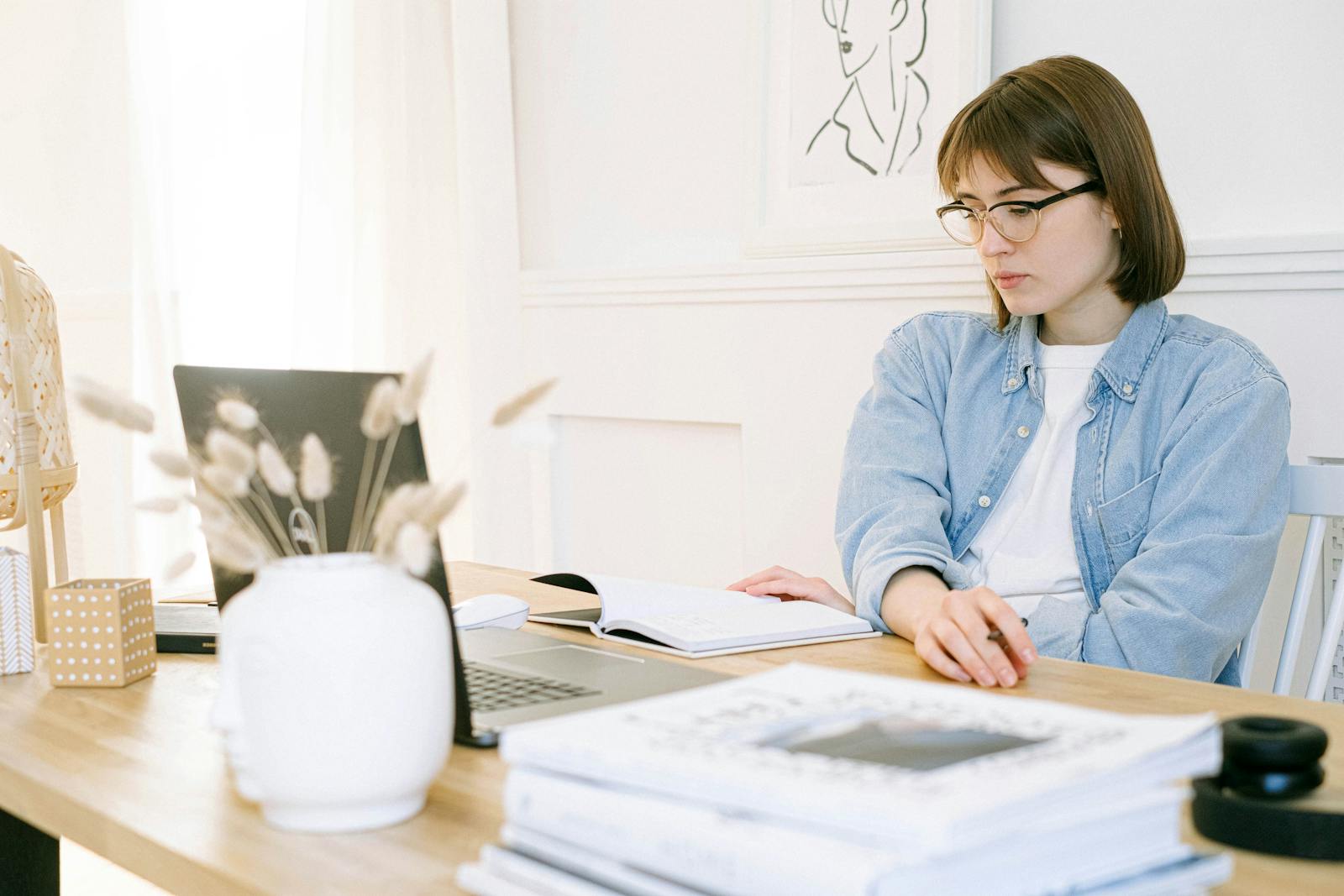Woman working in a stylish home office, taking notes with laptop open on desk.