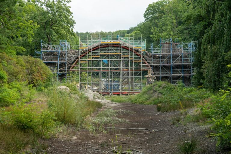 Scaffolding surrounds Rakotzbrücke in Kromlau Park during reconstruction. Lush green forest backdrop.