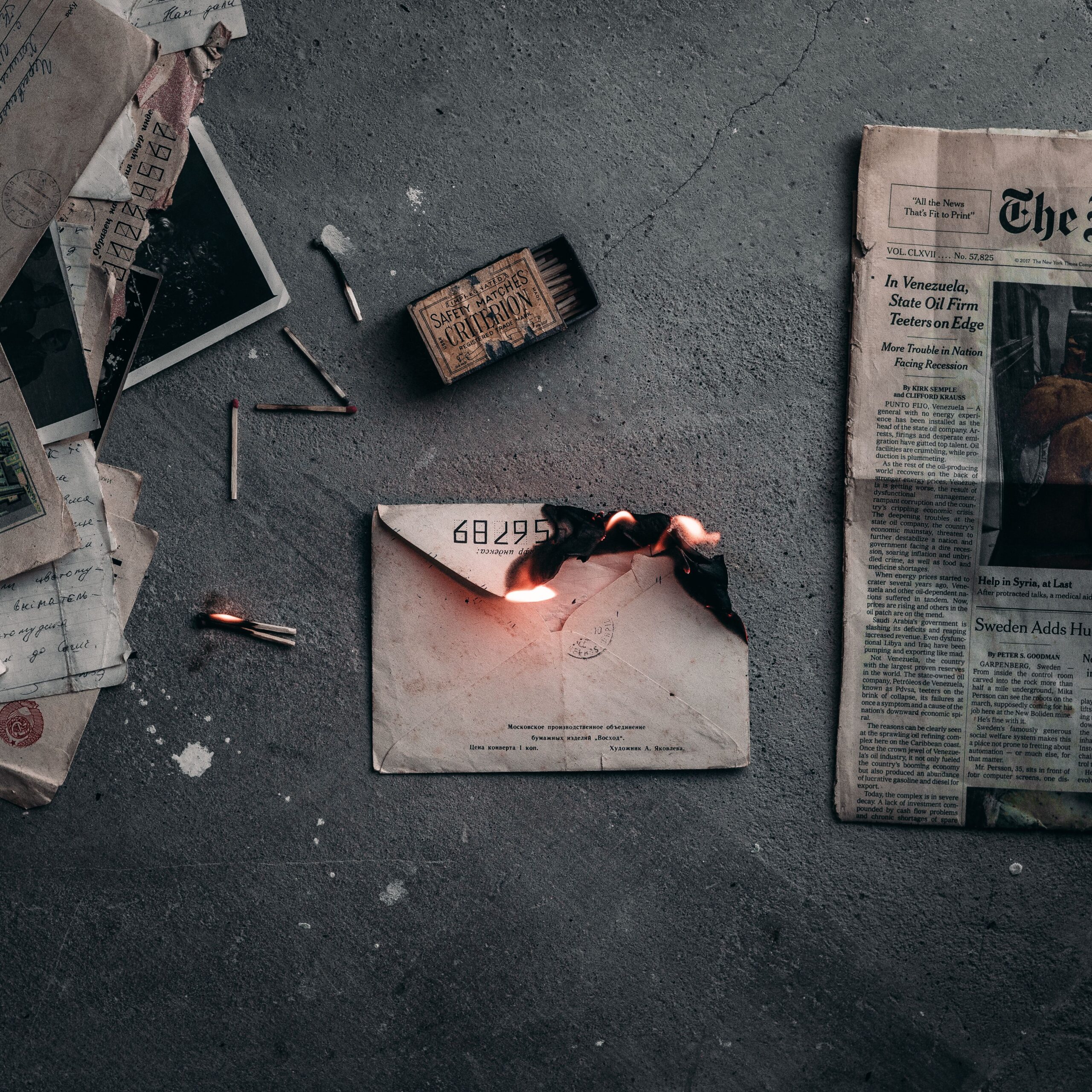 A dramatic scene of a burning envelope surrounded by matchsticks and old papers on a concrete floor.