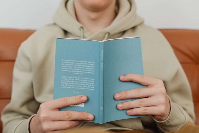 Close-up of hands holding a hardcover book, wearing a beige hoodie. Ideal for reading-related content.
