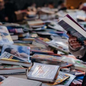 A person browsing books at a crowded market book sale, offering a variety of genres and selections.